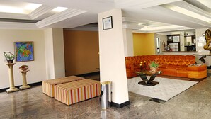 Eine Hotellobby mit Marmorboden, einer gestreiften Bank, einem orangefarbenen Sofa und zwei farbenfrohen Bildern an der Wand.