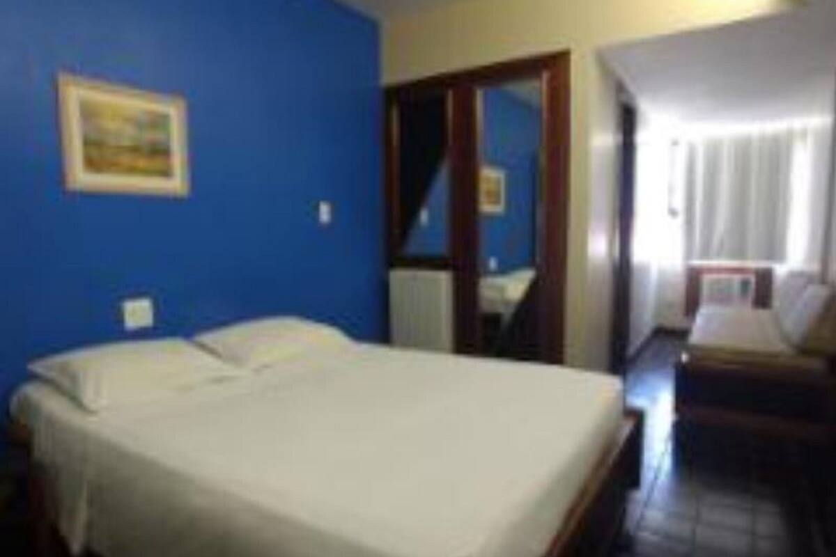 Habitación de hotel con cama, una mesita pequeña y una silla. Se ve una ventana con cortinas y una puerta que da a otra habitación.