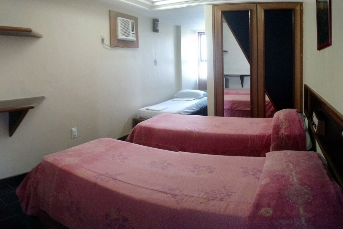 Une petite chambre compacte avec deux lits simples, un bureau avec un ordinateur et un petit réfrigérateur.