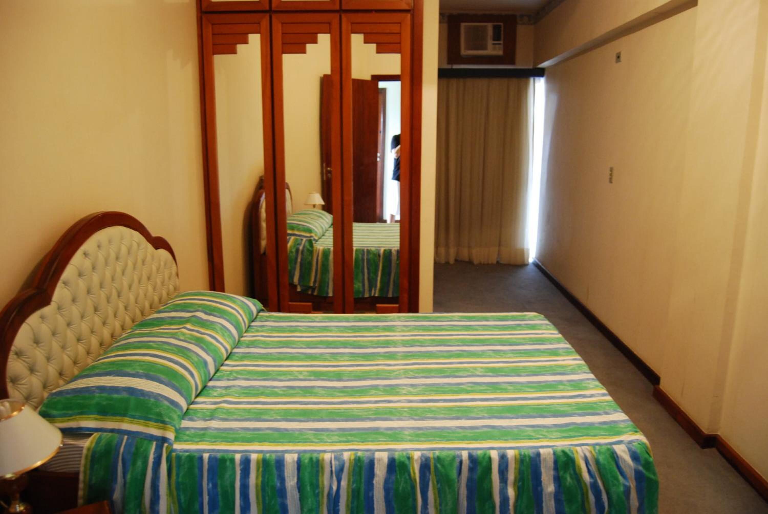 Ein Hotelzimmer mit Bett, Holzschrank, Spiegel und einem Flur mit Vorhang.