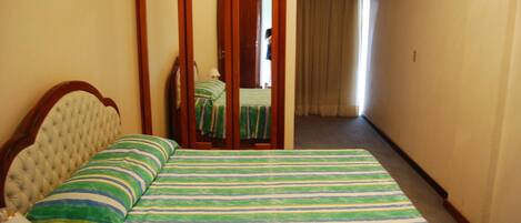 Ein Hotelzimmer mit Bett, Holzschrank, Spiegel und einem Flur mit Vorhang.
