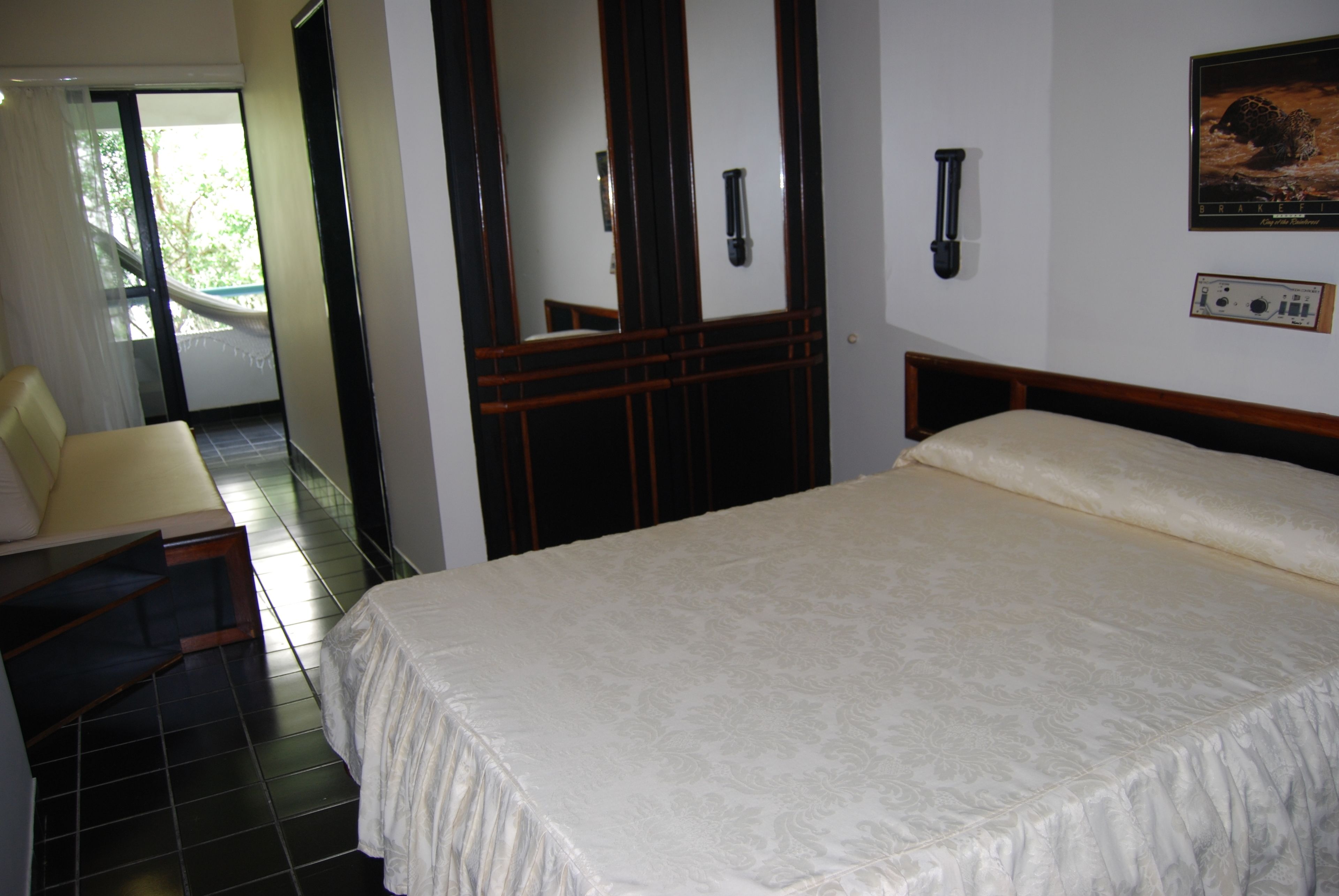 Quarto de hotel com uma cama grande, uma escrivaninha com cadeira, banheiro com espelho e vista para o exterior.
