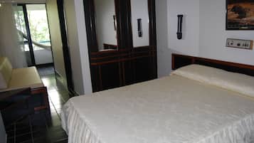 A hotel room with a large bed, a desk with a chair, a bathroom with a mirror, and a view of the outdoors.