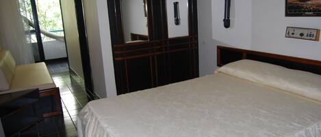 Quarto de hotel com uma cama grande, uma escrivaninha com cadeira, banheiro com espelho e vista para o exterior.