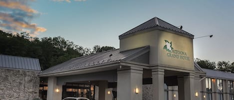 A hotel entrance with a stone facade, a covered driveway, and a white car parked in front.
