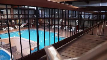 A pool area with a wooden deck and white chairs.
