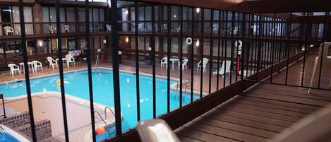 A pool area with a wooden deck and white chairs.