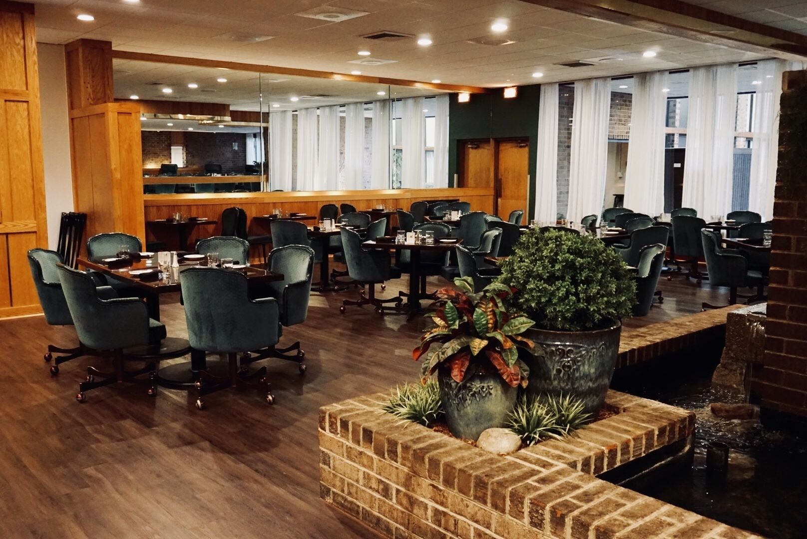 A conference room with multiple tables and chairs, a brick planter with plants, and a brick wall.