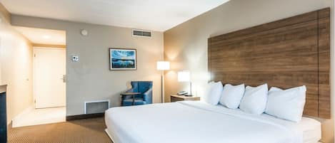A hotel room with a large bed, a desk, a chair, a lamp, and a picture on the wall.