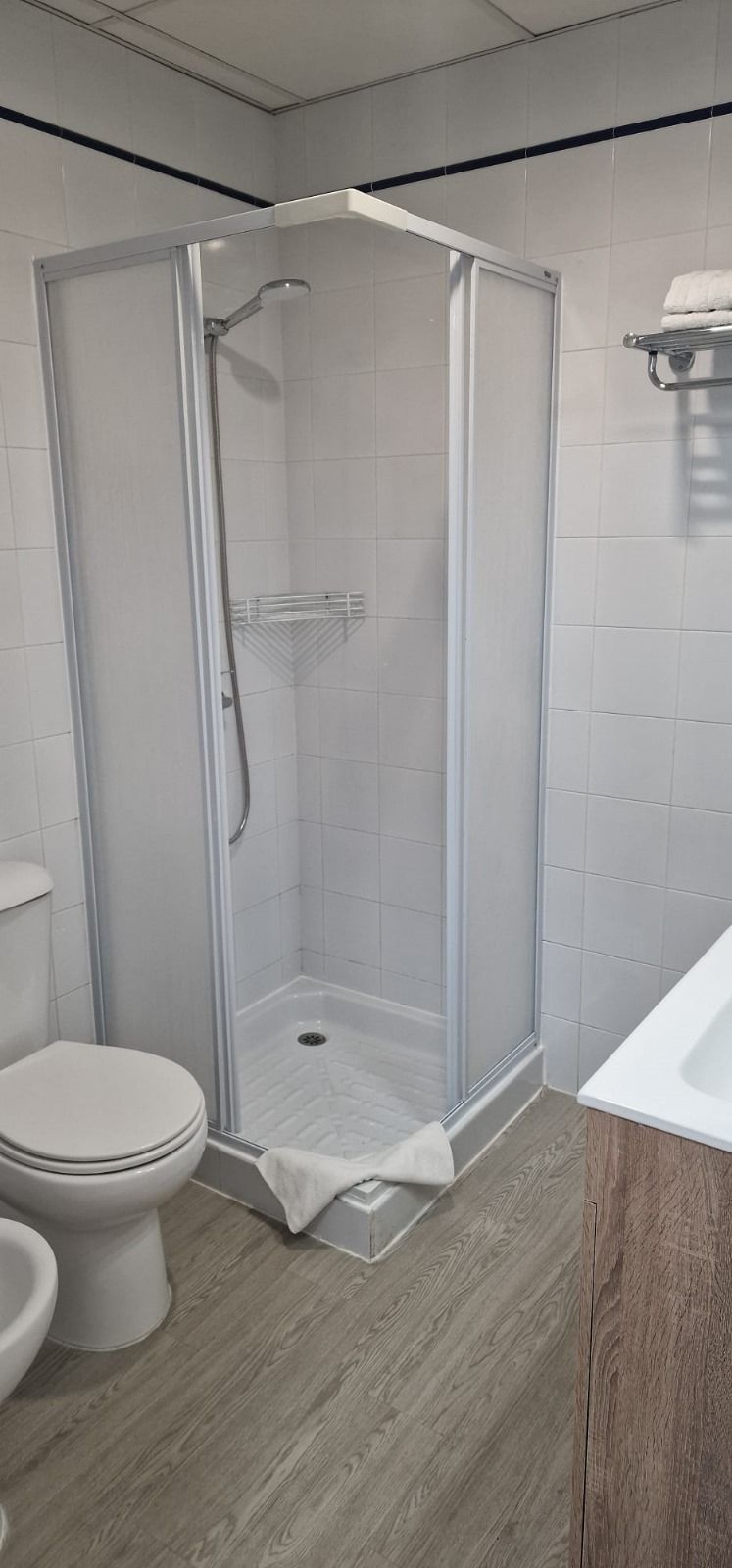 Un baño moderno con ducha de vidrio, inodoro blanco y tocador de madera.