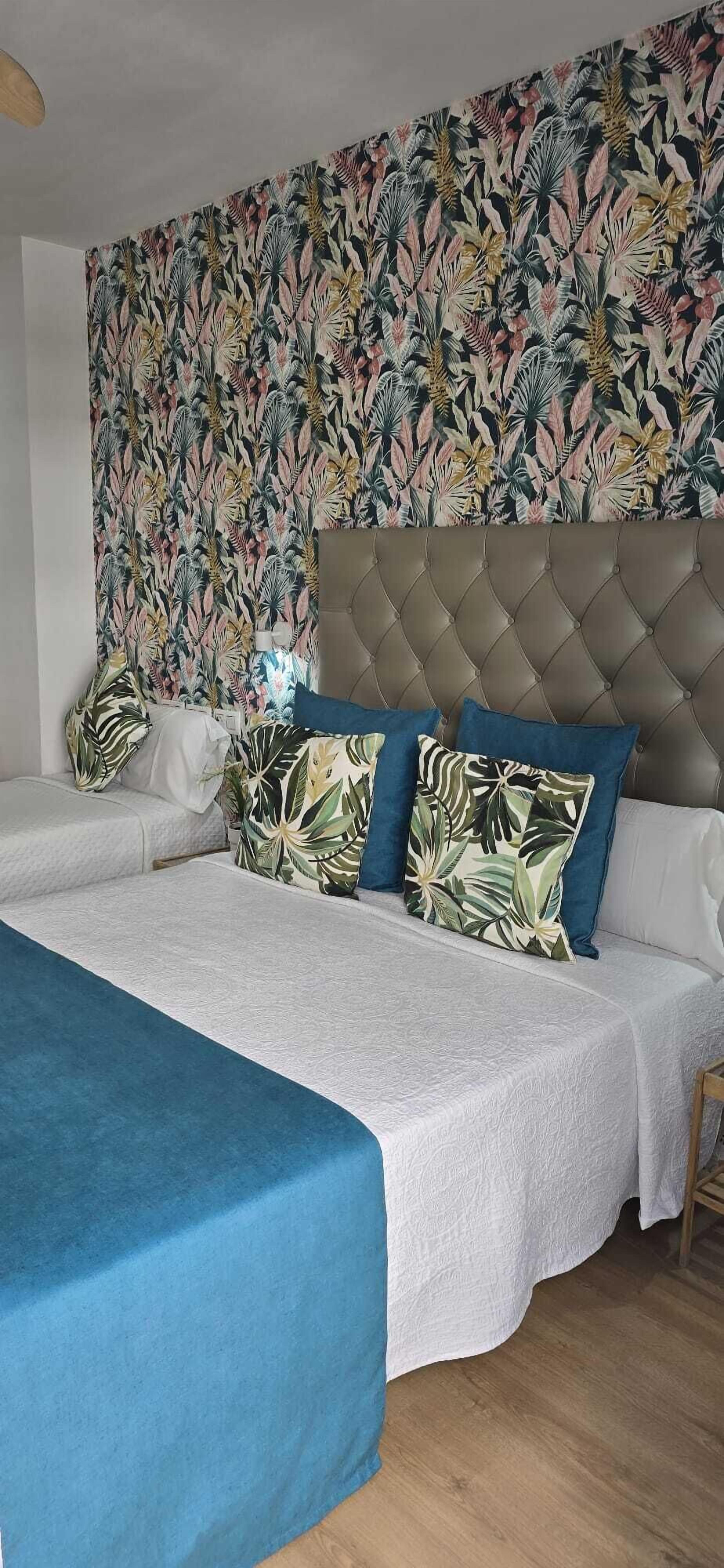 A bedroom with a large bed, a tufted headboard, and a tropical leaf-patterned wallpaper.