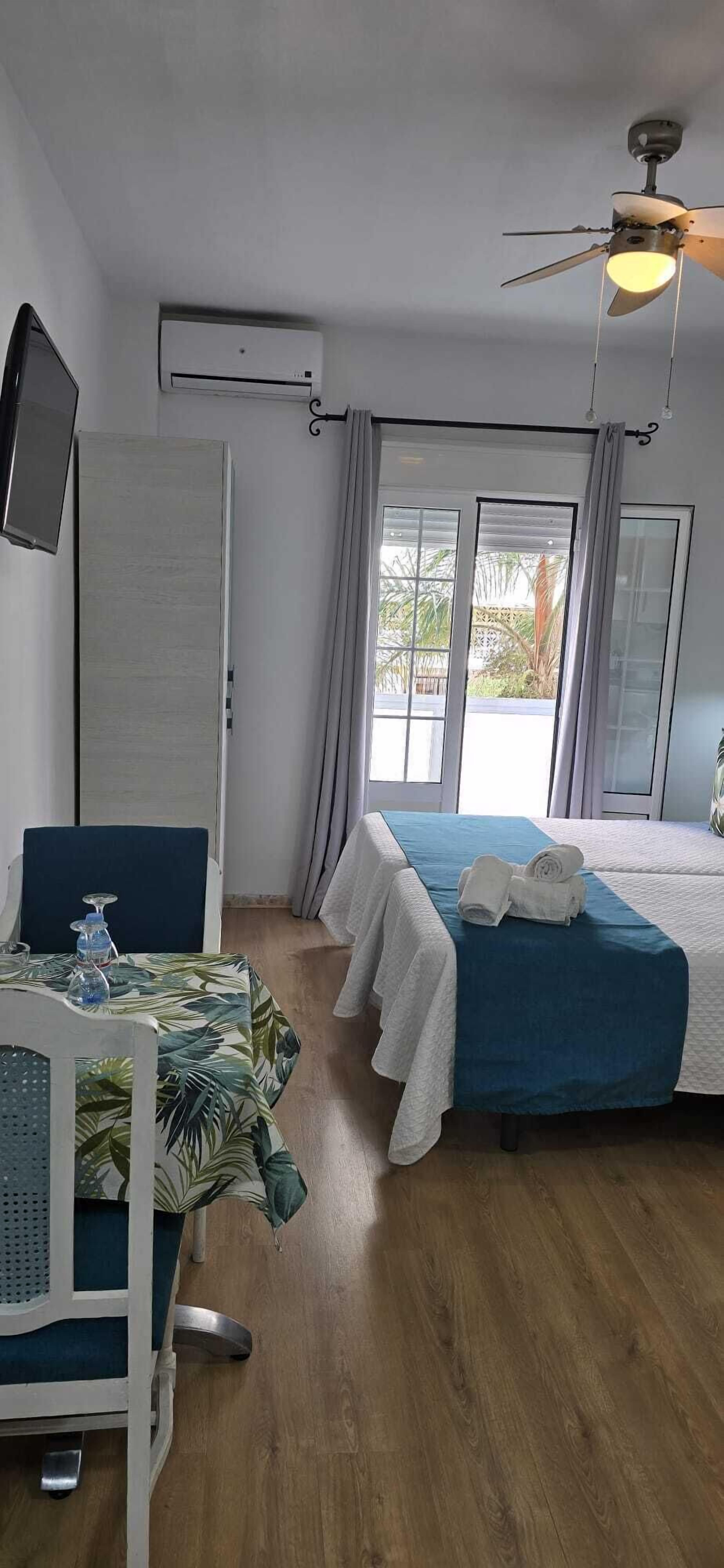 Een hotelkamer met een bed, bureau, stoel, airconditioning en plafondventilator, met uitzicht op de omgeving.