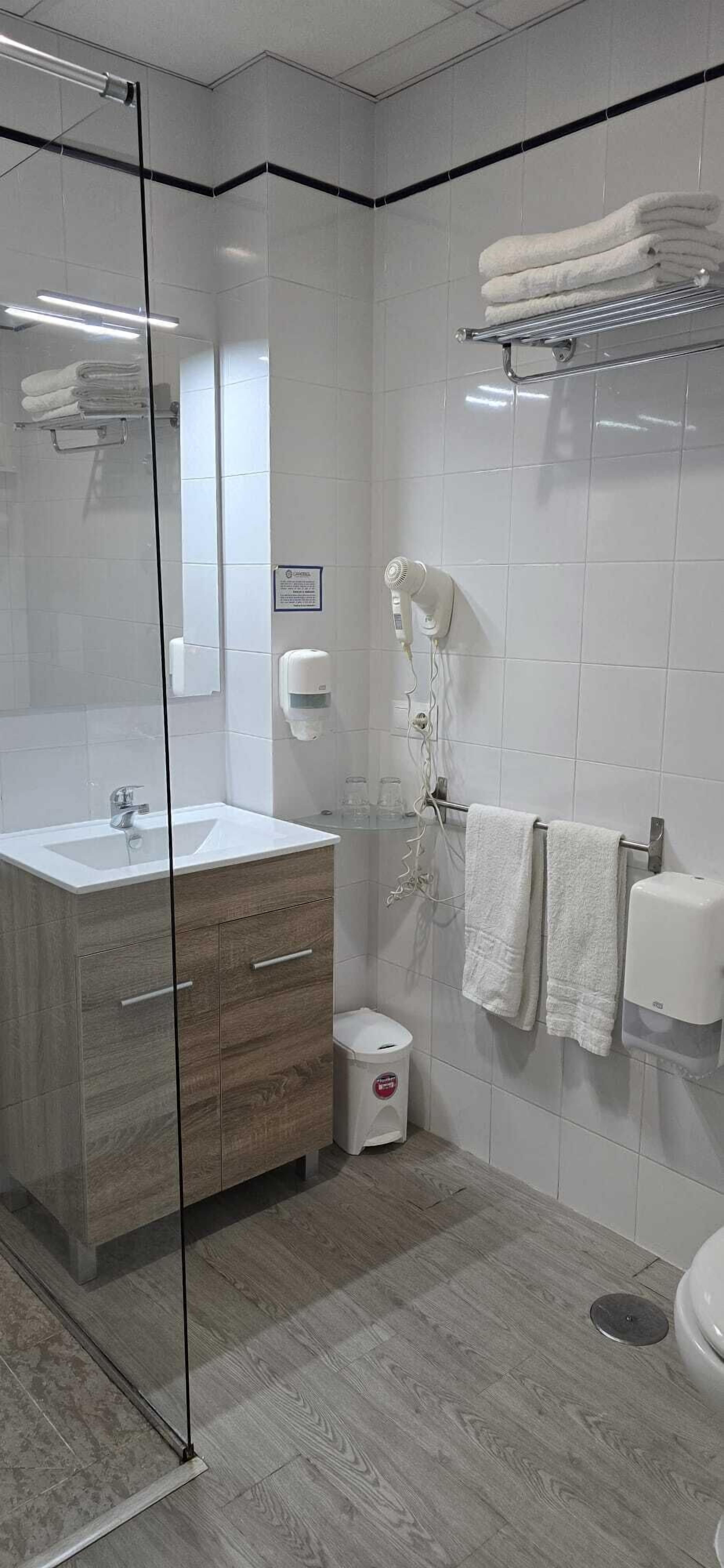 A modern bathroom with a glass shower enclosure, a sink with a wooden vanity, a hairdryer, and a towel rack.