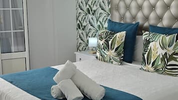 A bedroom with a tufted headboard, a bed with a blue and white bedspread, and a tropical leaf-patterned wallpaper.