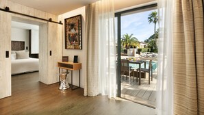 Una habitación de hotel moderna con piso de madera, una cama, un escritorio y vista a un área de piscina al aire libre.