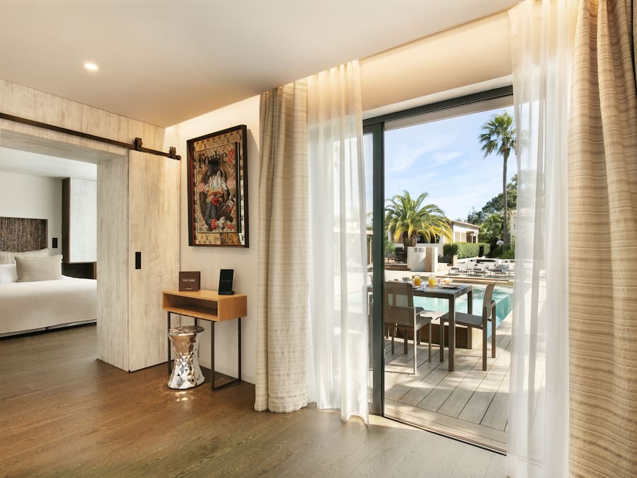 Una habitación de hotel moderna con piso de madera, una cama, un escritorio y vista a un área de piscina al aire libre.