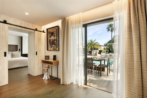 Una habitación de hotel moderna con piso de madera, una cama, un escritorio y vista a un área de piscina al aire libre.
