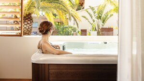 Una mujer relajándose en un jacuzzi con vista a palmeras y un edificio al exterior.
