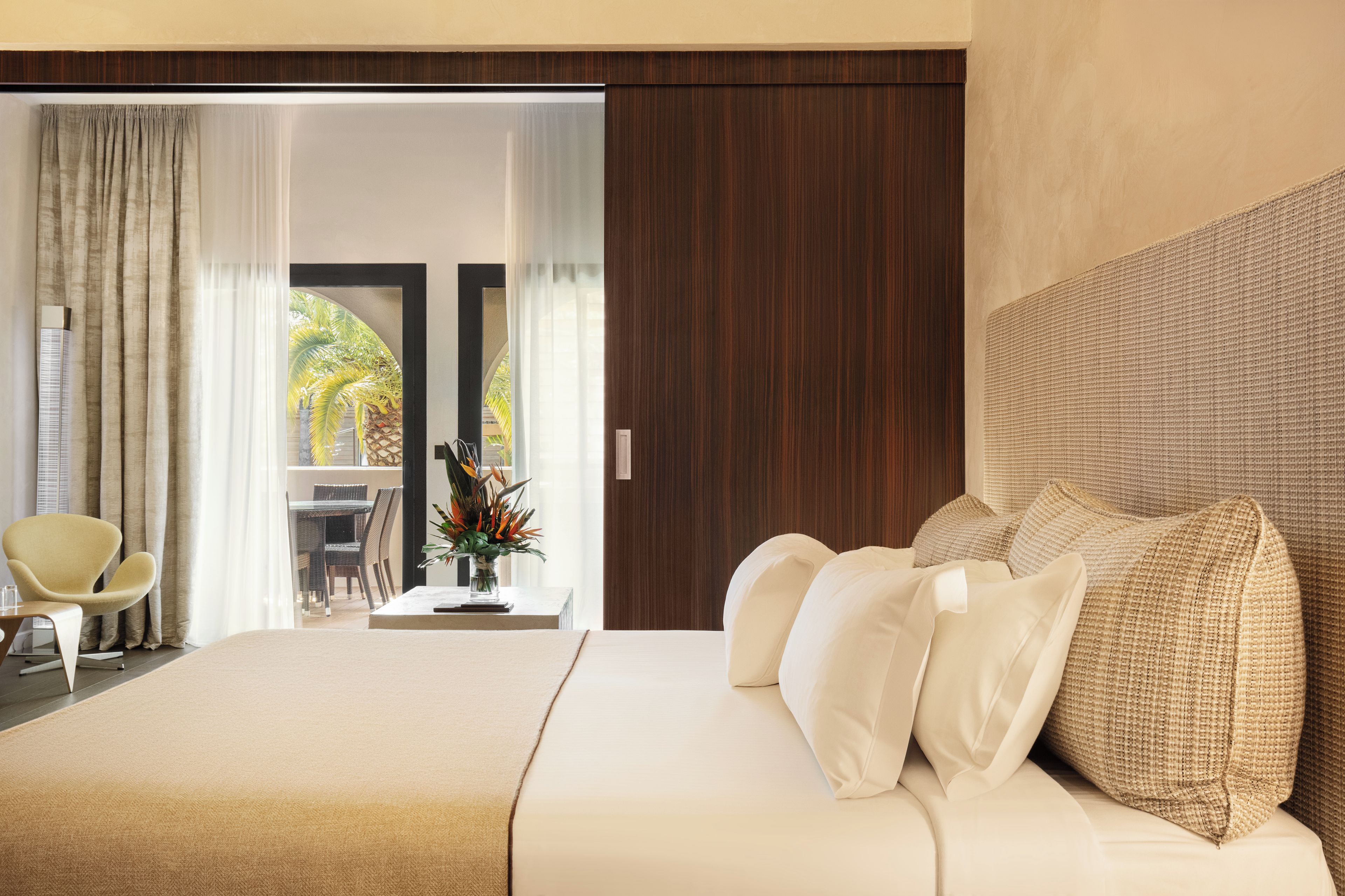 Ein modernes Hotelzimmer mit einem großen Bett, einer Sitzecke mit einem Sessel, einem kleinen Tisch und Blick ins Freie.