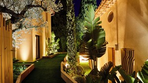 Un sendero iluminado en un jardín con cerca de madera, diversas plantas y un muro de ladrillo.