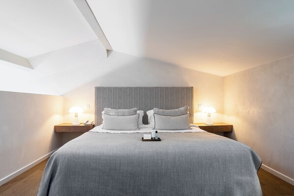 Una habitación de hotel moderna con una cama grande, dos mesitas de noche con lámparas y suelo de madera.