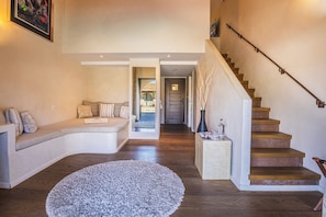 Amplia sala de estar con una escalera de madera, una zona de estar con un banco y vista al comedor.