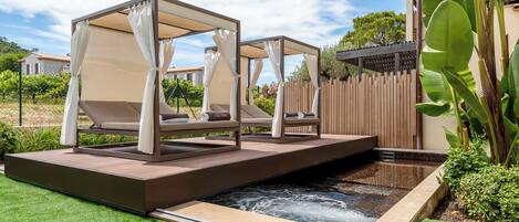 A spa area with two outdoor beds, a small pool, and lush greenery.