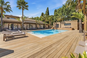 Une terrasse en bois avec une piscine, des chaises longues et des palmiers.