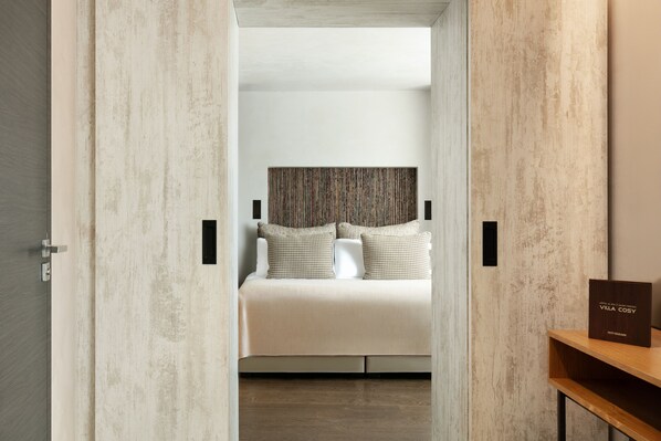A modern bedroom with a bed, a textured headboard, and a wooden nightstand with a book. - Hôtel Villa Cosy (Saint-Tropez)