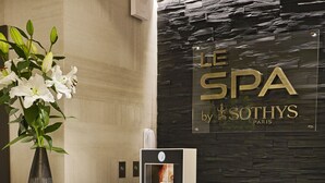 A reception area with a modern reception desk, a vase with white flowers, and a wall with the text "LE SPA by SOTHYS PARIS". - Hôtel Villa Cosy (Saint-Tropez)