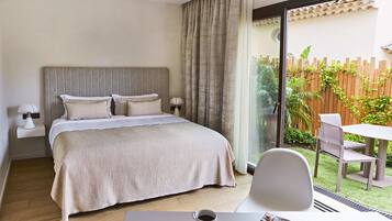 Habitación de hotel con cama, una mesa con taza y cuchara, y vista a un patio con mesa y sillas.