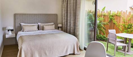 A hotel room with a bed, a table with a cup and a spoon, and a view of a patio with a table and chairs.