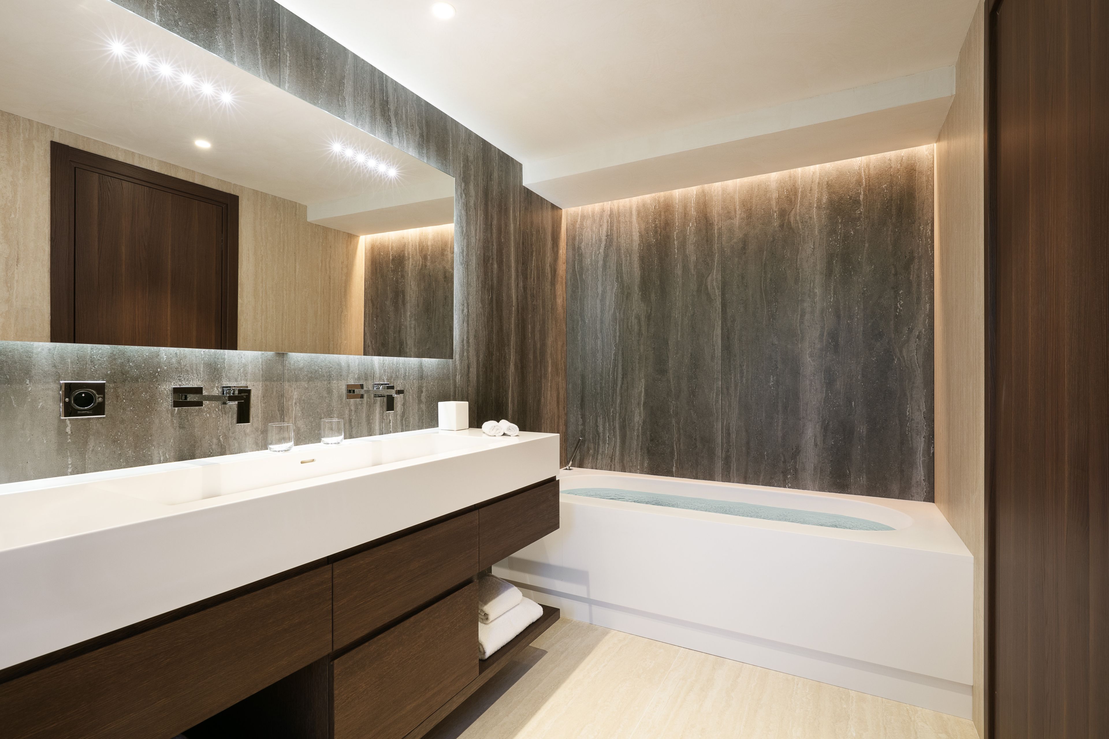 A modern bathroom with a large mirror, a white sink, and a bathtub.