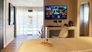 Habitación de hotel con cama, escritorio, silla, televisor en la pared y vistas al exterior.