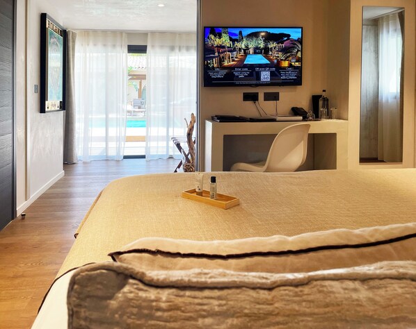 A hotel room with a bed, a desk, a chair, a TV on the wall, and a view of the outdoors. - Hôtel Villa Cosy (Saint-Tropez)