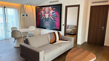 A modern living room with a sofa, coffee table, TV, and a dining area with chairs and a table.
