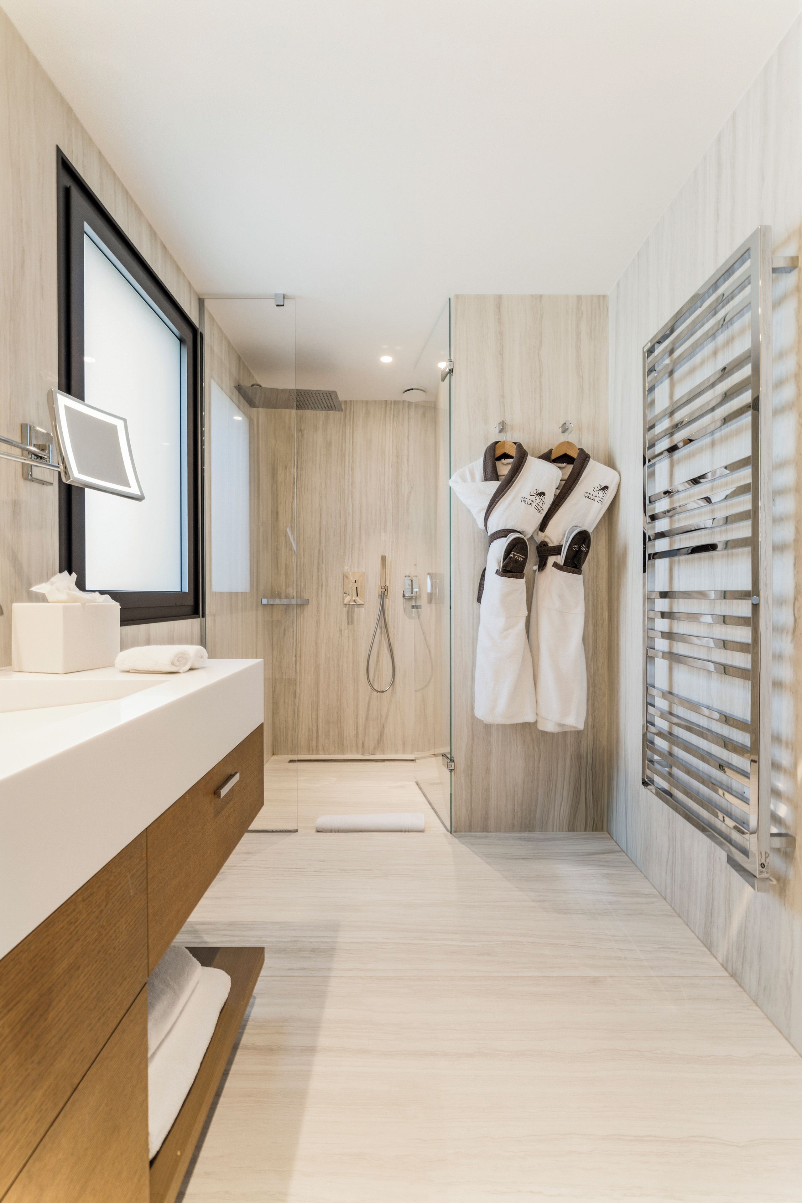 A modern bathroom with a large mirror, a shower, and a towel rack with robes.