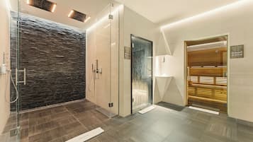 A modern bathroom with a glass shower enclosure, a stone wall, and a wooden door.