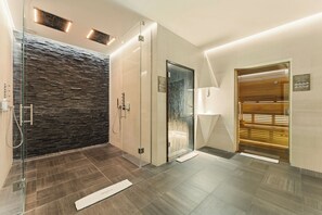 Un baño moderno con cabina de ducha de vidrio, pared de piedra y puerta de madera.