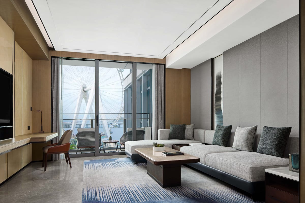 Una sala de estar moderna con un sofá, una mesa de centro y un televisor. Hay un ventanal con vistas a un edificio y una grúa.