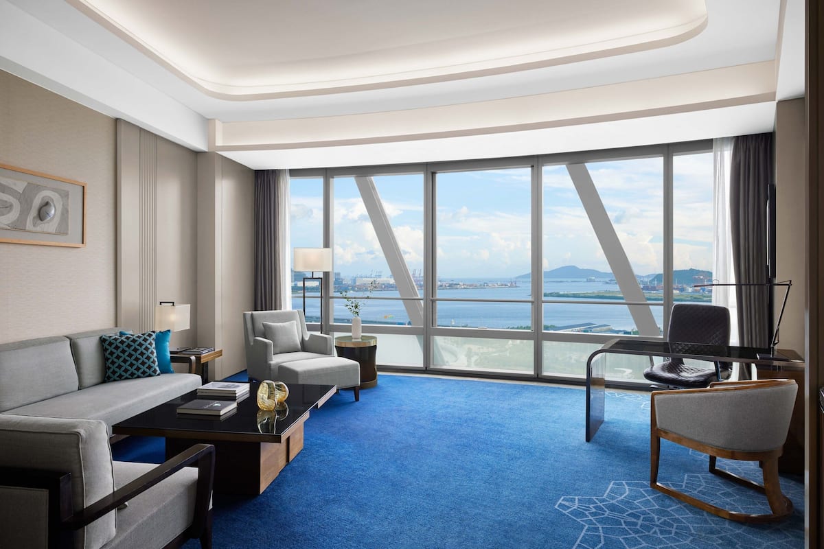 Habitación de hotel moderna con un amplio ventanal que ofrece vistas a la ciudad, un sofá, un escritorio y una silla.