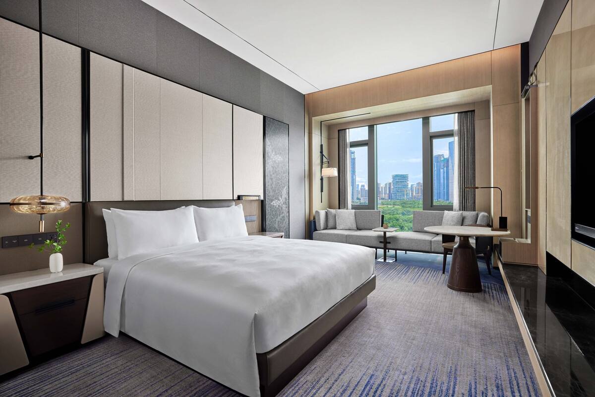 Una habitación de hotel moderna con una cama grande, un sofá, una mesa de comedor y vistas a la ciudad.