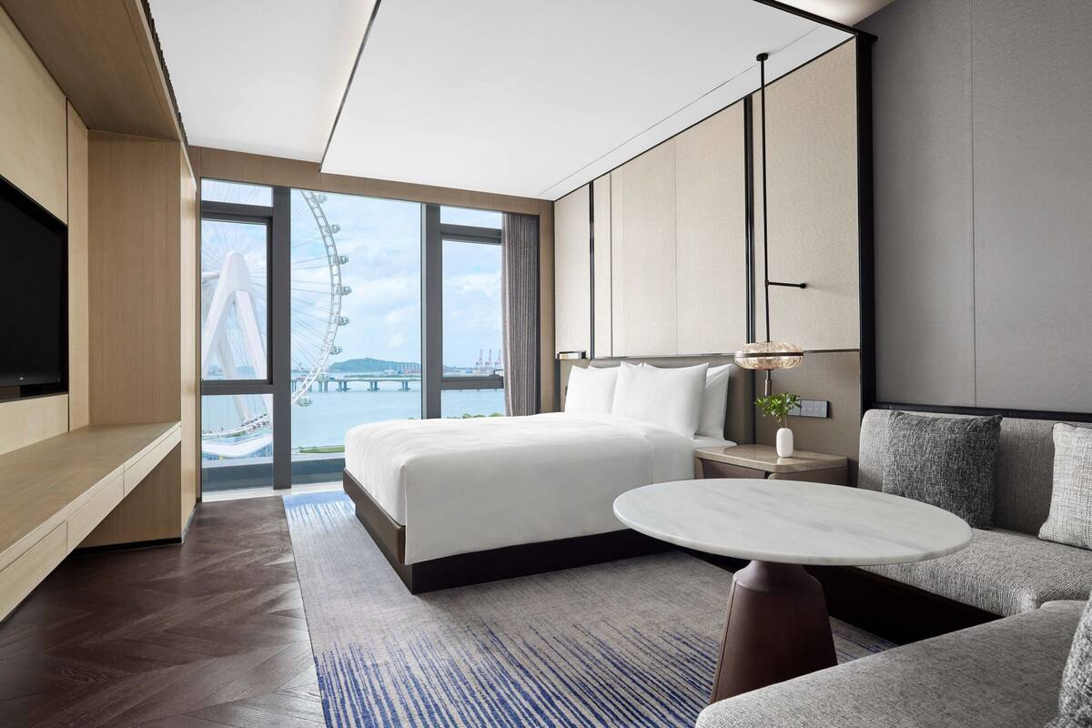 Una habitación de hotel moderna con una cama grande, un sofá, un televisor y vistas a una noria.