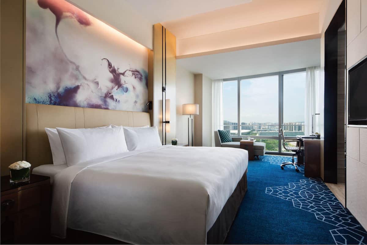 Habitación de hotel con una cama grande, un escritorio, una silla, un televisor y un ventanal con vistas a la ciudad.