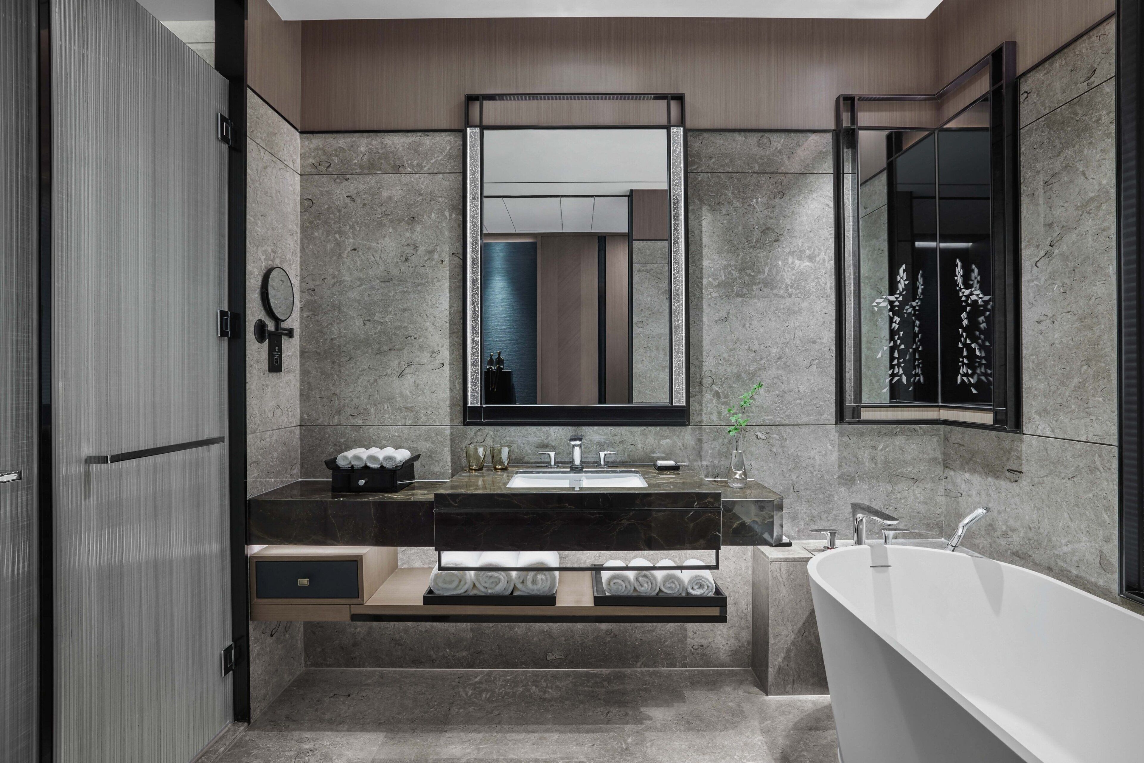 Un baño moderno con una bañera independiente, un espejo grande y una encimera de mármol.
