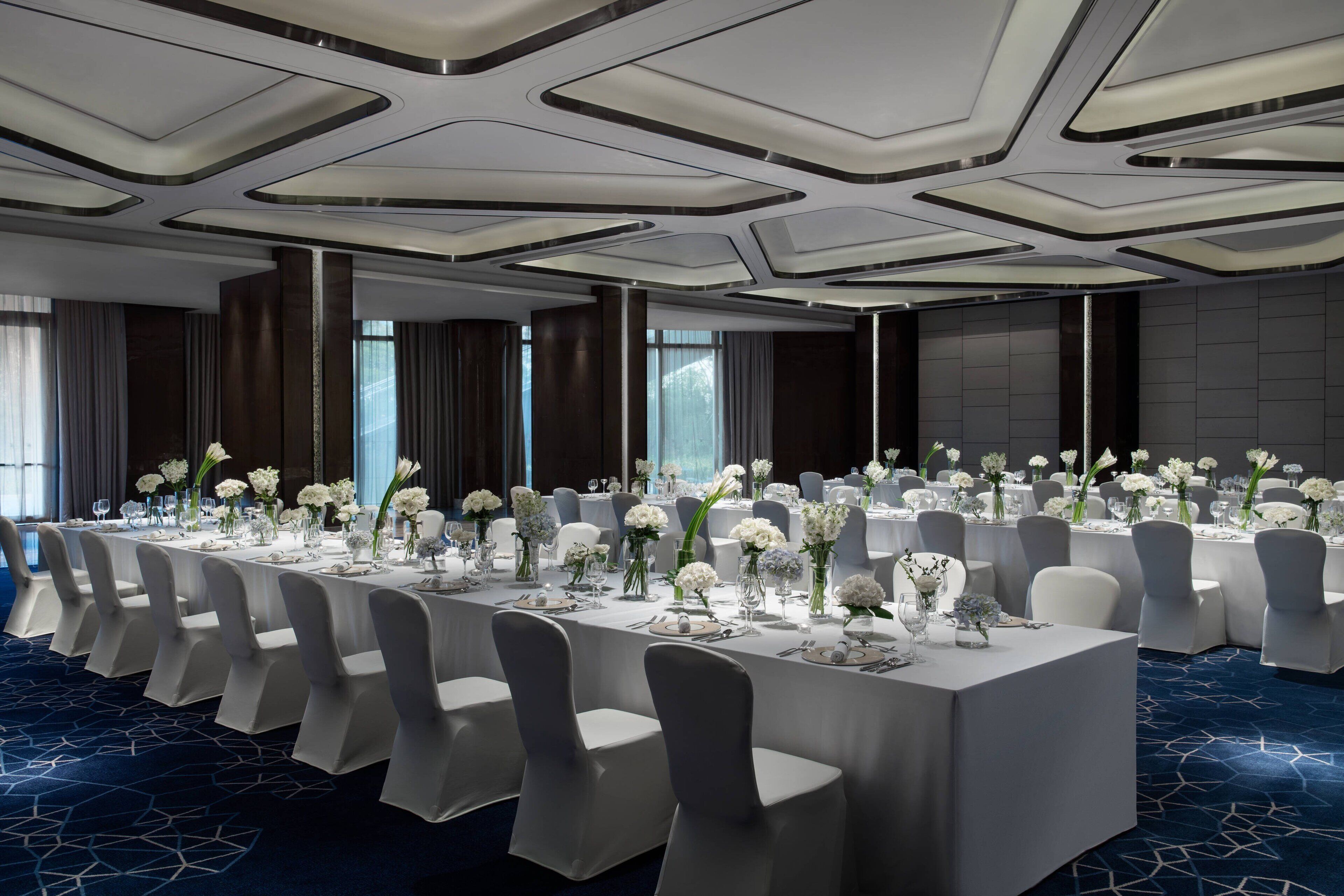 A banquet hall with a long table set for a formal event, surrounded by chairs.