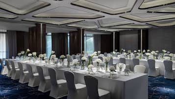 A banquet hall with a long table set for a formal event, surrounded by chairs.