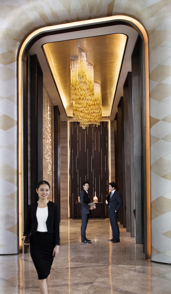 A modern lobby with a large chandelier, polished marble floors, and a geometric wall design.