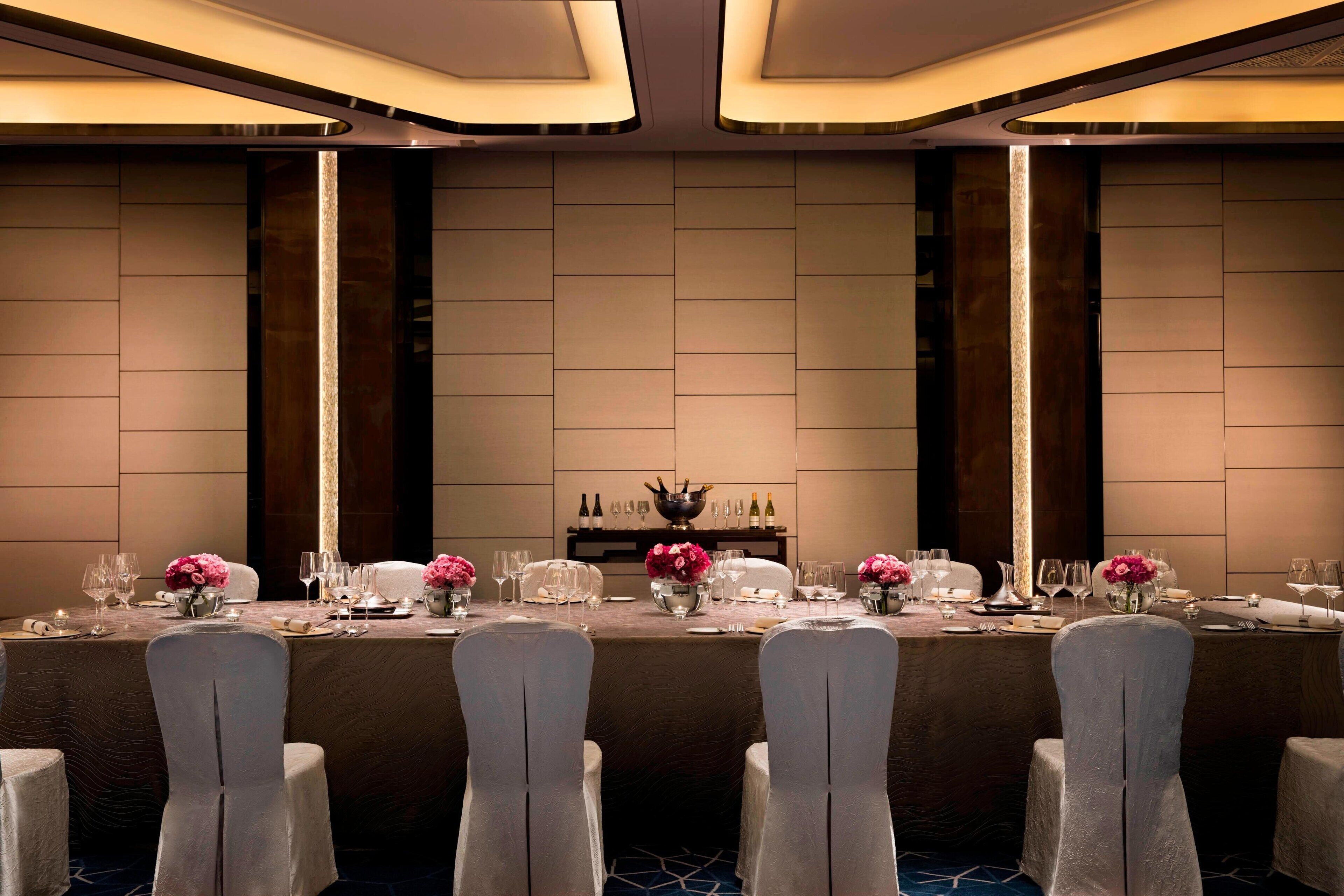 A formal dining room with a long table set for a meal, flanked by tall, narrow chairs.