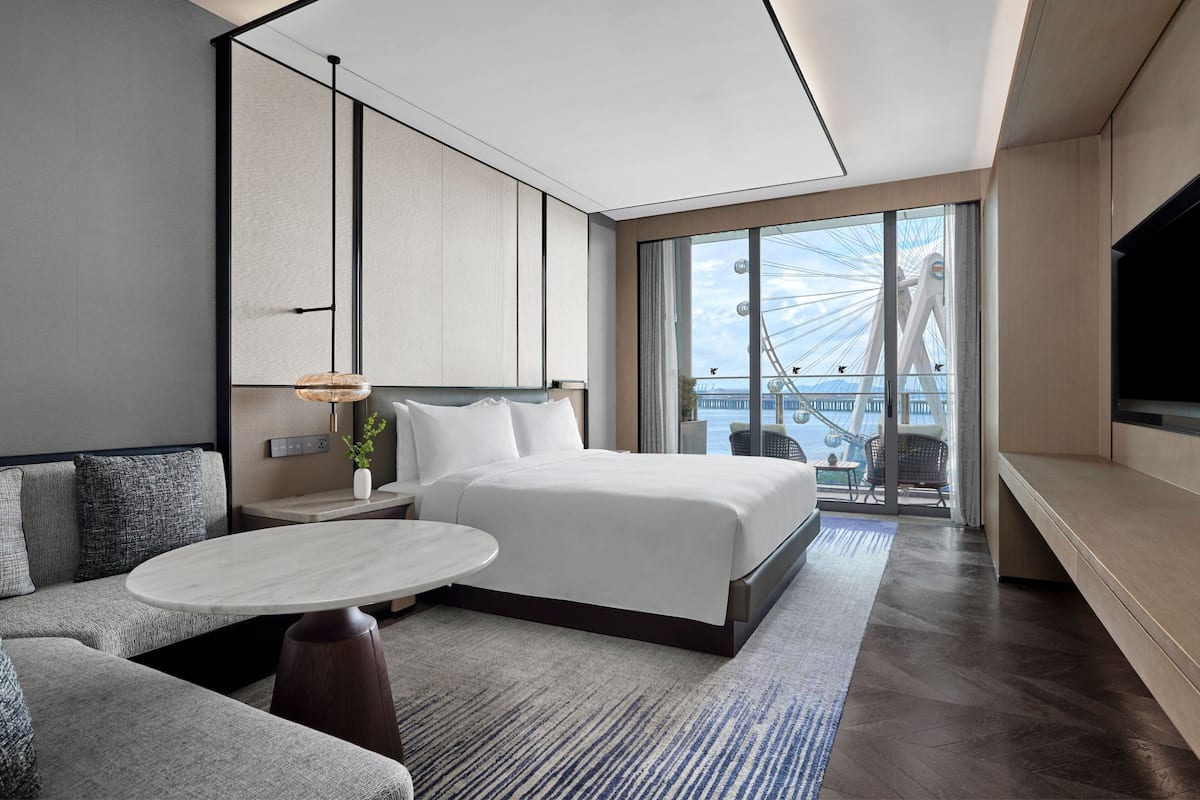 Una habitación de hotel moderna con una cama grande, un espacio de descanso con una mesa redonda y vistas a una noria a través de un ventanal amplio.